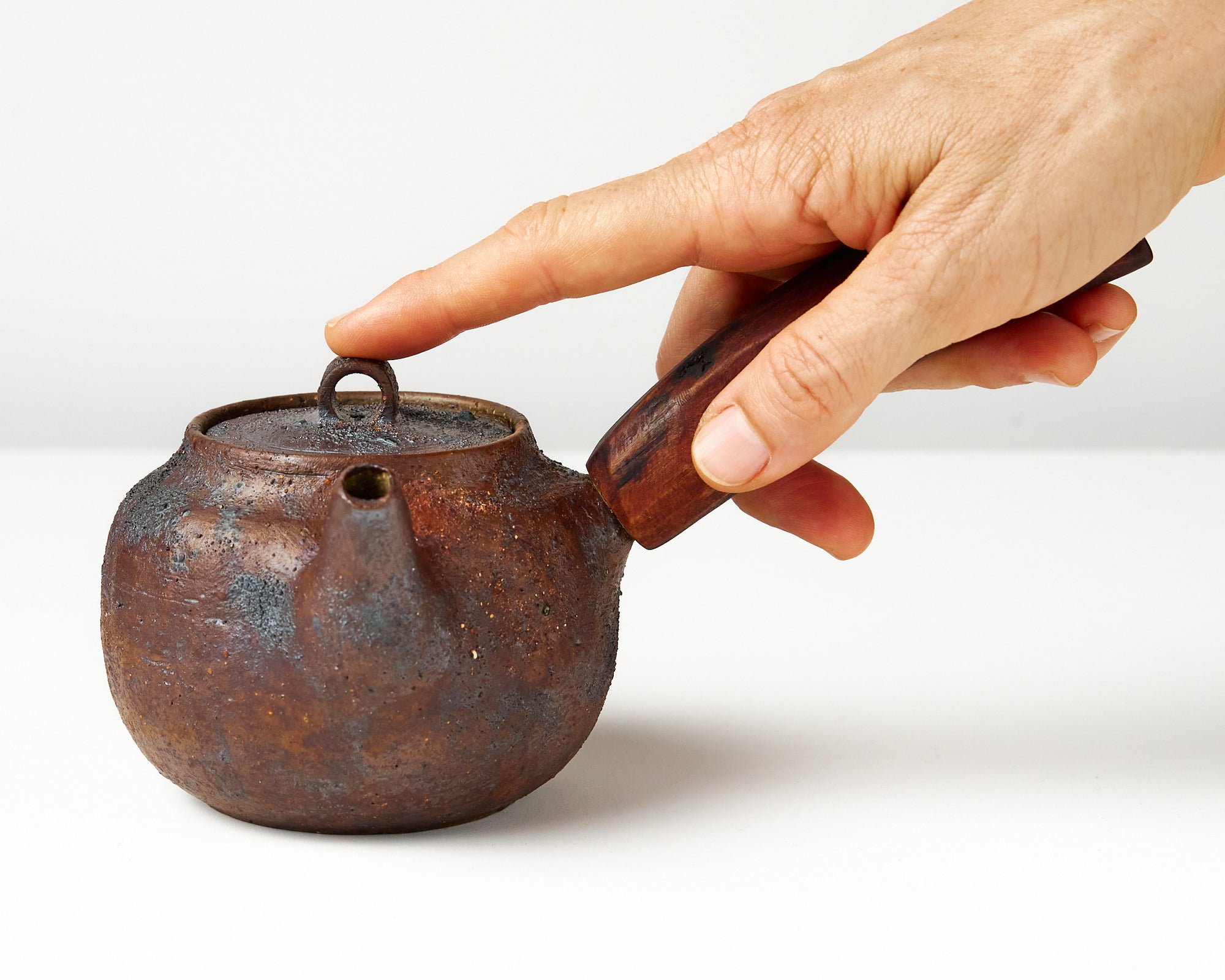 Side handle tea pot with wooden handle on white background. front view with hand to show scale