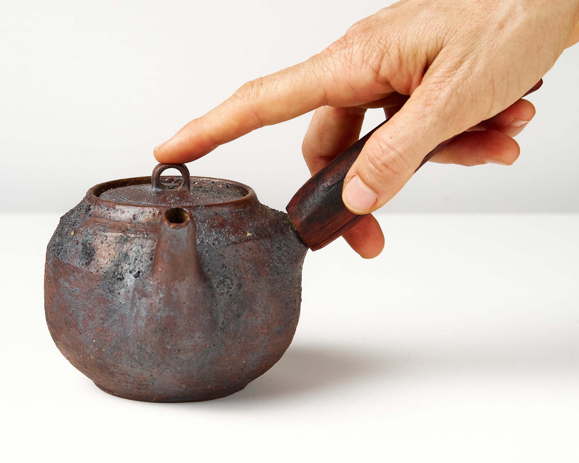 Side handle tea pot with wooden handle on white background. front view with hand to show scale