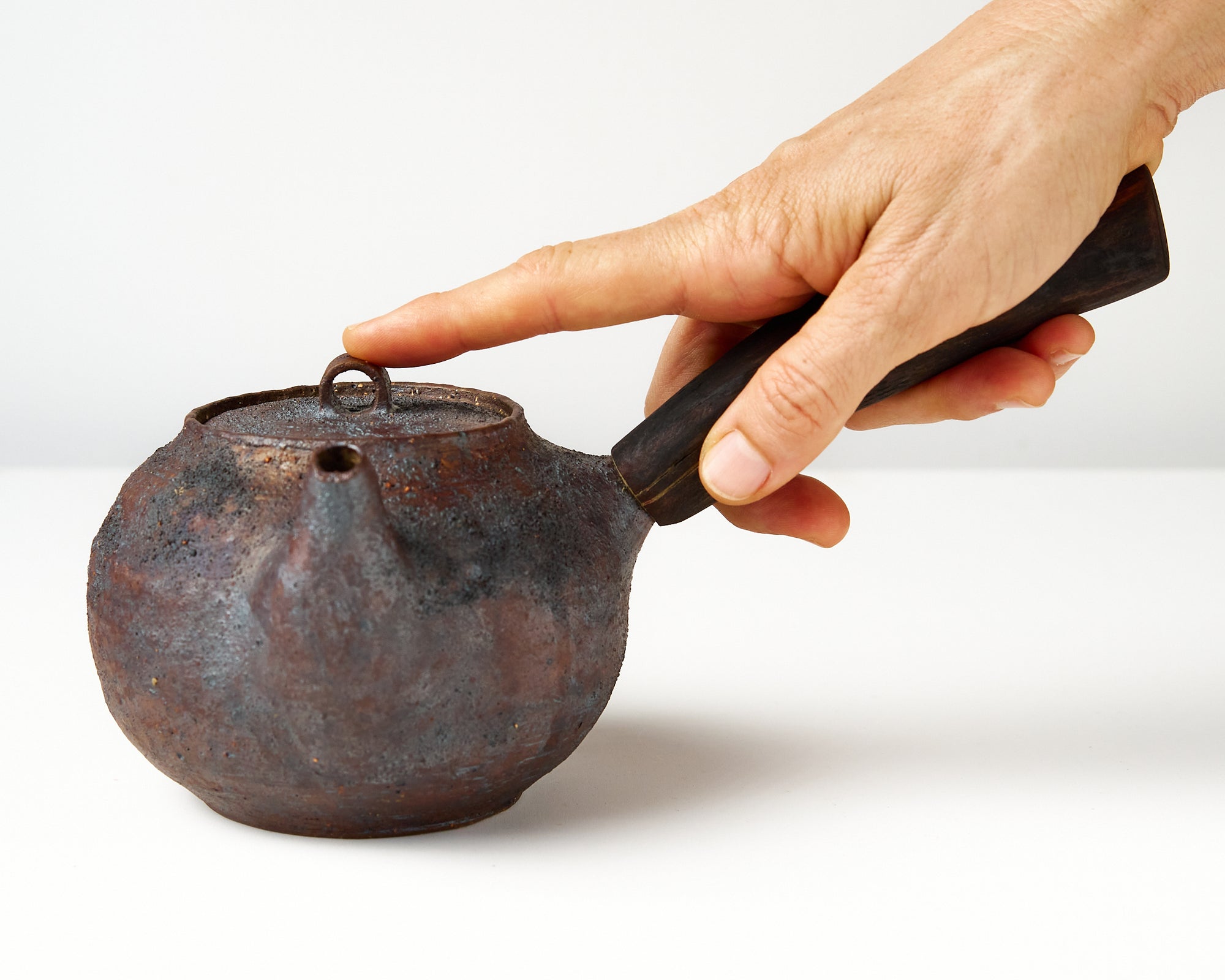 Side handle tea pot with wooden handle on white background. front view with hand to show scale