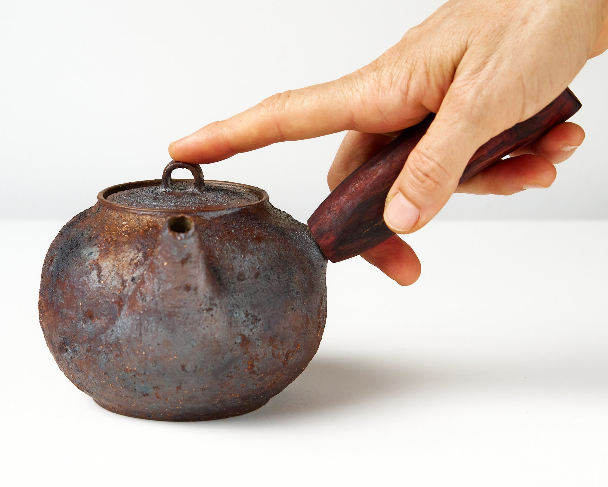 Side handle tea pot with wooden handle on white background. front view with hand to show scale
